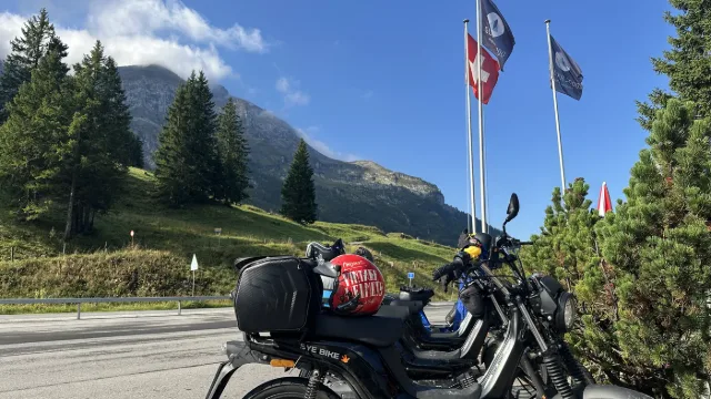 Un motorino davanti a un villaggio di montagna con bandiere.