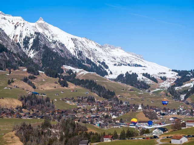 Château-d'Œx im Tal, darüber Heissluftballone.