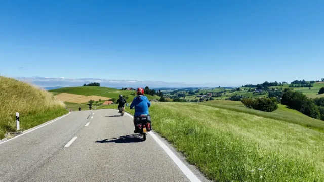 Ein Töfflifahrer auf einer Hügelstrasse mit Blick auf die Alpen.